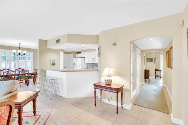 kitchen with white fridge with ice dispenser, white cabinets, kitchen peninsula, backsplash, and light tile patterned flooring