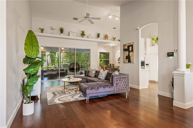 living room with a high ceiling, decorative columns, ceiling fan, and dark hardwood / wood-style floors