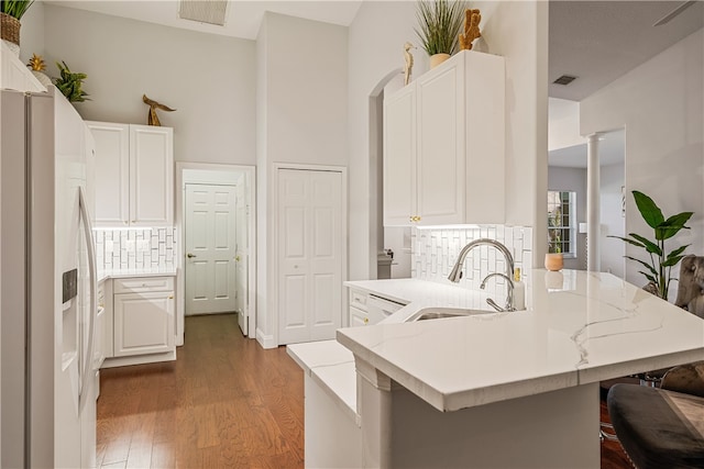 kitchen featuring a kitchen bar, tasteful backsplash, sink, white cabinetry, and white fridge with ice dispenser