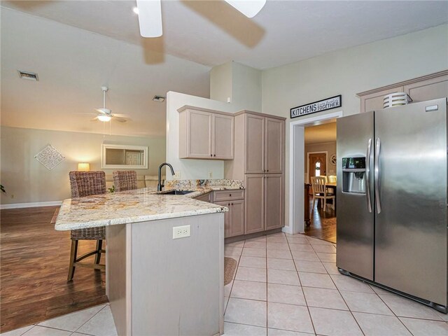 kitchen featuring sink, stainless steel fridge with ice dispenser, kitchen peninsula, a kitchen bar, and light tile patterned floors