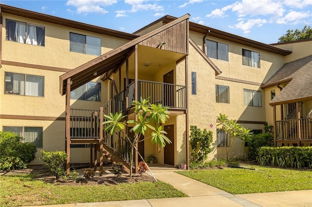 view of front facade featuring a balcony, a front yard, and stucco siding