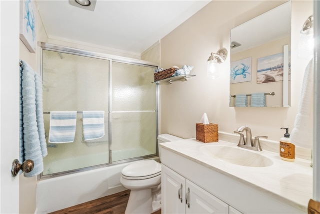 full bathroom with hardwood / wood-style floors, vanity, toilet, and bath / shower combo with glass door