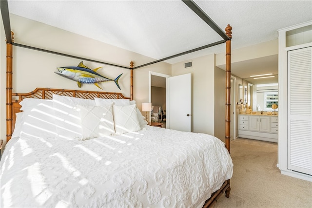 bedroom with connected bathroom, a textured ceiling, and light colored carpet