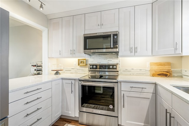 kitchen featuring appliances with stainless steel finishes, light stone countertops, decorative backsplash, hardwood / wood-style flooring, and white cabinets