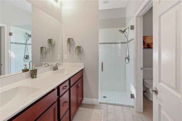 bathroom featuring double vanity, toilet, a stall shower, and a sink