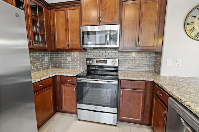 kitchen featuring light stone counters, decorative backsplash, glass insert cabinets, and appliances with stainless steel finishes