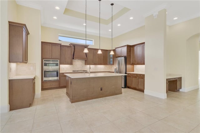 kitchen featuring hanging light fixtures, appliances with stainless steel finishes, a center island with sink, and a tray ceiling