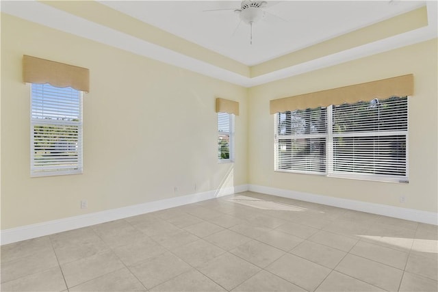 empty room featuring ceiling fan, a raised ceiling, and light tile patterned floors