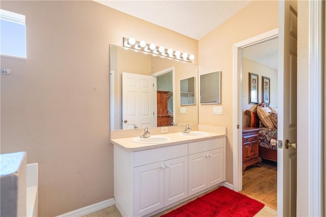 bathroom featuring a sink, baseboards, double vanity, and ensuite bathroom