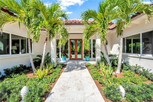 view of exterior entry with french doors, a tiled roof, and stucco siding