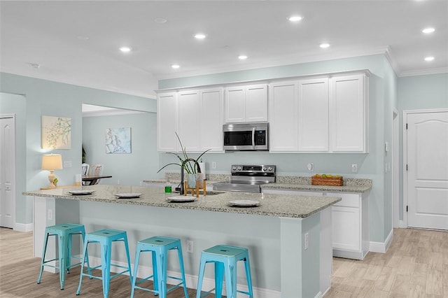 8645 95th Ave, Vero Beach, FL 32967 - kitchen featuring appliances with stainless steel finishes, crown molding, light wood-style flooring, a kitchen breakfast bar, and white cabinets