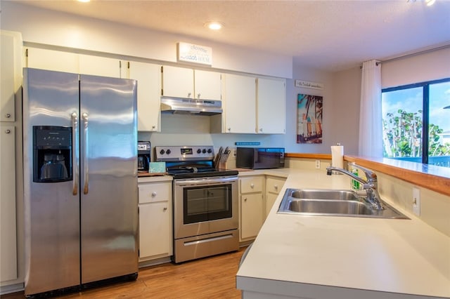 kitchen with appliances with stainless steel finishes, sink, white cabinets, a textured ceiling, and light hardwood / wood-style flooring