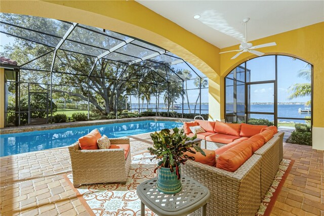 view of pool with an outdoor living space, ceiling fan, a water view, glass enclosure, and a patio area