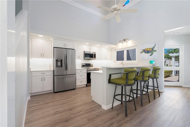 kitchen featuring appliances with stainless steel finishes, a towering ceiling, white cabinetry, a kitchen bar, and light hardwood / wood-style flooring