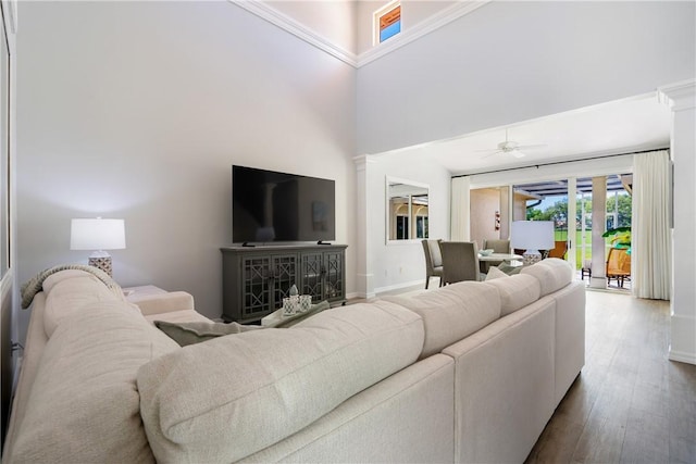 living room featuring hardwood / wood-style flooring, decorative columns, ceiling fan, and a towering ceiling