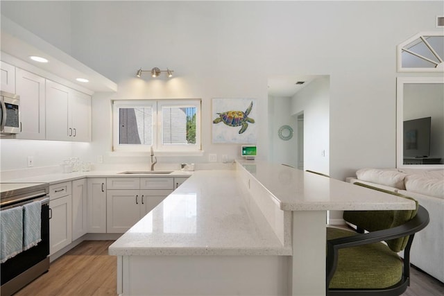 kitchen featuring sink, light hardwood / wood-style flooring, white cabinetry, stainless steel appliances, and a kitchen breakfast bar