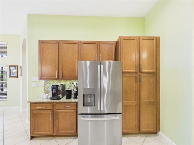 kitchen featuring light tile patterned floors, stainless steel fridge with ice dispenser, brown cabinets, and baseboards