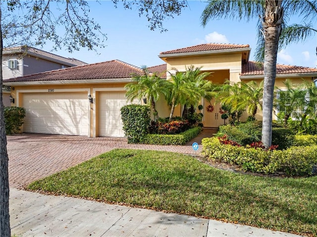 mediterranean / spanish-style home with a front yard, stucco siding, a garage, a tiled roof, and decorative driveway