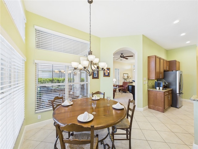 dining room featuring light tile patterned floors, ceiling fan with notable chandelier, arched walkways, and baseboards