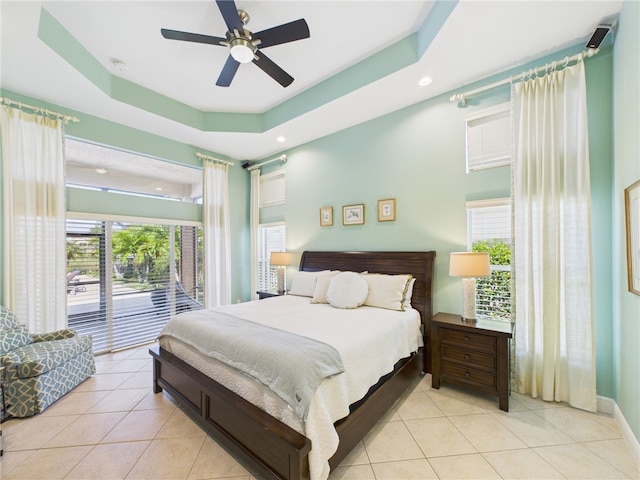 bedroom with light tile patterned floors, multiple windows, a tray ceiling, and access to outside