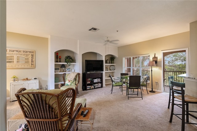 carpeted living room featuring built in shelves and ceiling fan