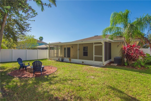 back of property with an outdoor fire pit, a lawn, cooling unit, and a sunroom