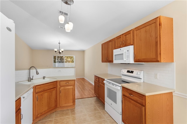 kitchen with pendant lighting, white appliances, backsplash, sink, and a notable chandelier