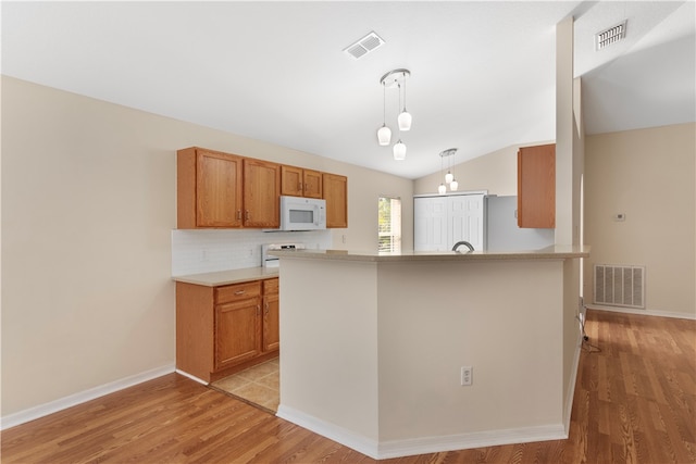 kitchen with vaulted ceiling, pendant lighting, light hardwood / wood-style floors, and white appliances