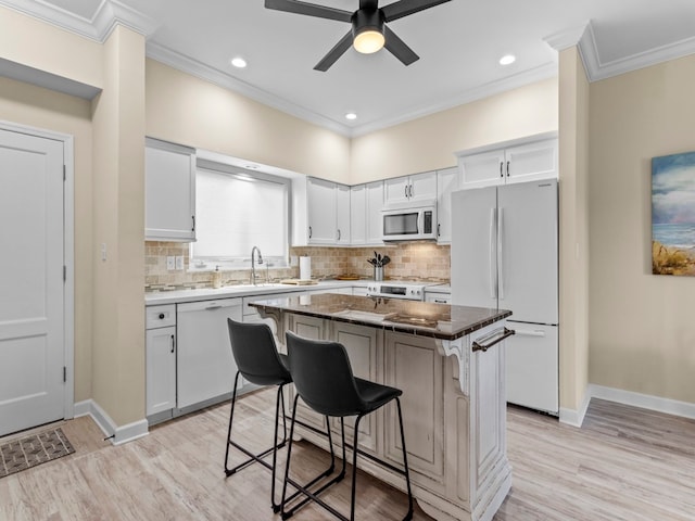 kitchen featuring a kitchen breakfast bar, white appliances, a kitchen island, white cabinets, and light wood-type flooring