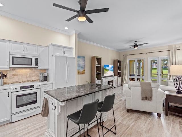 kitchen with white appliances, a kitchen bar, white cabinetry, and stone countertops