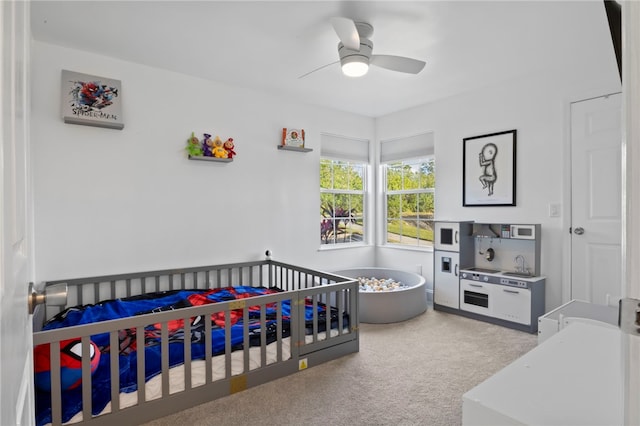 carpeted bedroom with a crib and ceiling fan