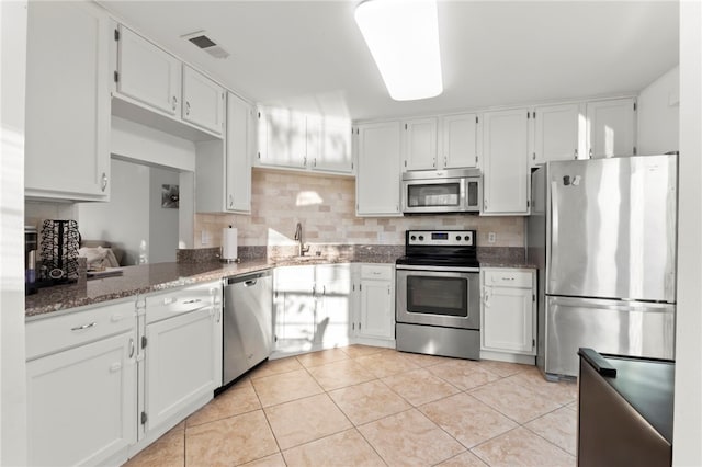 kitchen with sink, appliances with stainless steel finishes, white cabinetry, decorative backsplash, and dark stone counters