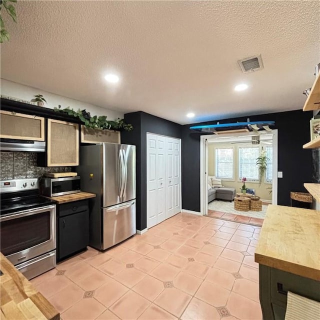 kitchen with wooden counters, a textured ceiling, light tile patterned floors, appliances with stainless steel finishes, and backsplash