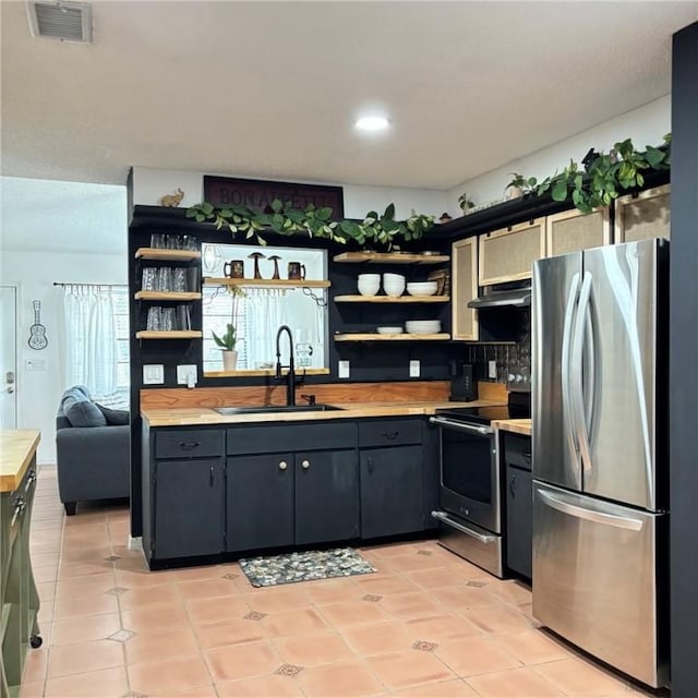 kitchen featuring butcher block counters, appliances with stainless steel finishes, sink, and light tile patterned floors