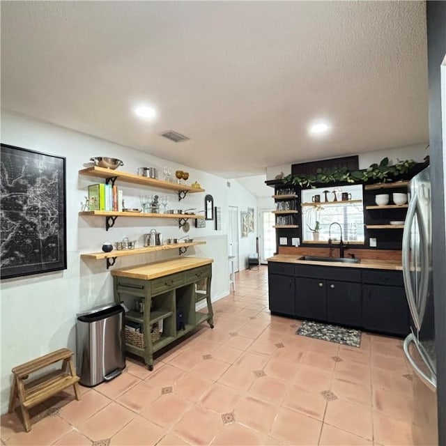 kitchen with stainless steel fridge, sink, a textured ceiling, and light tile patterned floors