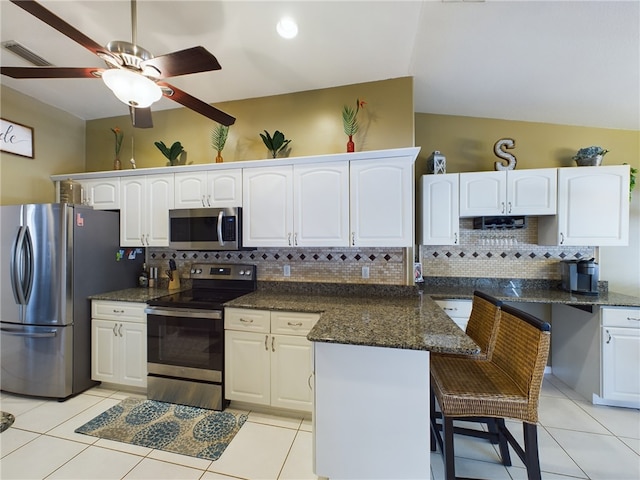 kitchen with appliances with stainless steel finishes, white cabinets, a kitchen breakfast bar, and dark stone counters