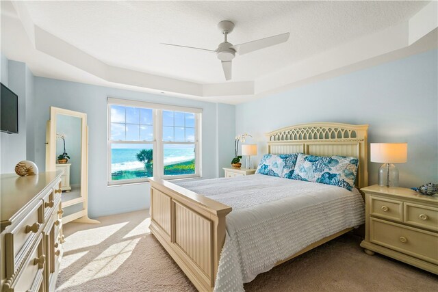 bedroom with ceiling fan, light carpet, and a tray ceiling