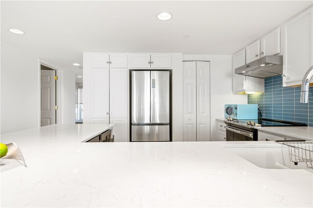 kitchen with decorative backsplash, light stone countertops, white cabinetry, and stainless steel refrigerator