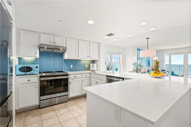 kitchen with kitchen peninsula, tasteful backsplash, stainless steel appliances, pendant lighting, and white cabinetry