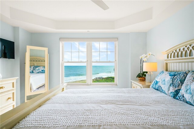 bedroom featuring a water view, a raised ceiling, and ceiling fan