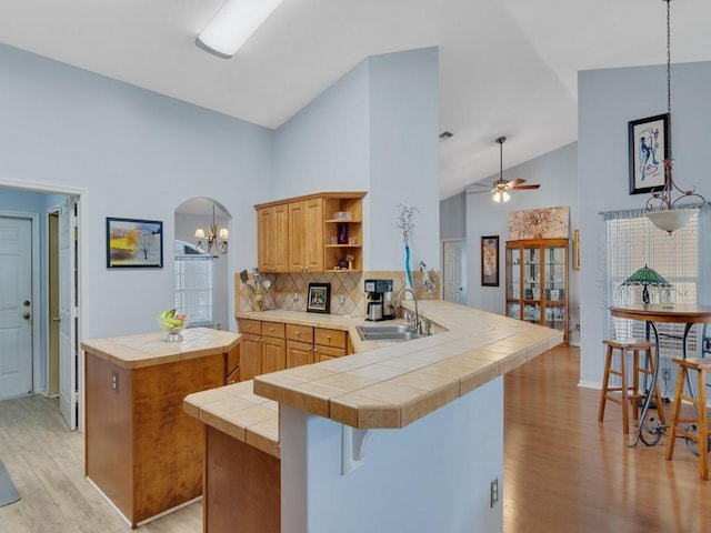 kitchen featuring light wood finished floors, tile counters, a peninsula, open shelves, and a sink