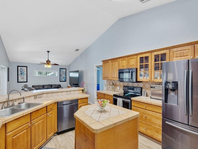 kitchen featuring tile counters, ceiling fan, appliances with stainless steel finishes, open floor plan, and a sink