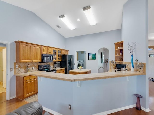 kitchen featuring visible vents, electric stove, independent washer and dryer, black refrigerator with ice dispenser, and stainless steel microwave