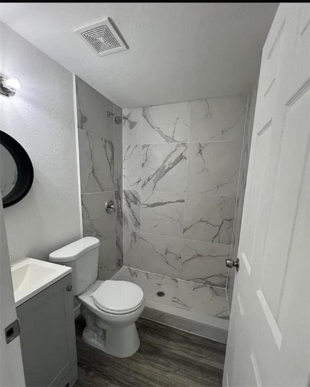 bathroom with tiled shower, vanity, hardwood / wood-style flooring, and toilet