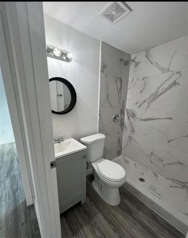 bathroom with tiled shower, hardwood / wood-style floors, vanity, and toilet