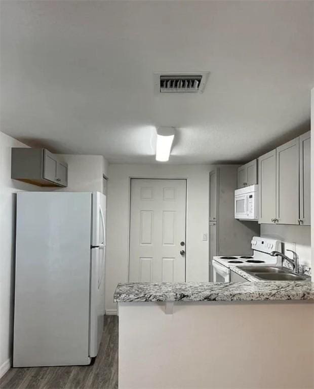 kitchen with kitchen peninsula, light stone counters, gray cabinetry, white appliances, and sink