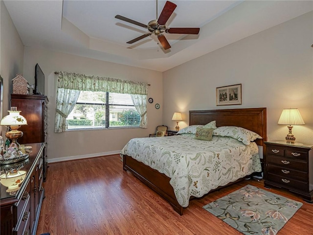 bedroom featuring hardwood / wood-style flooring, ceiling fan, and a raised ceiling