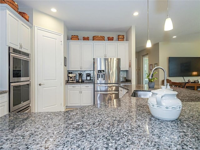 kitchen featuring appliances with stainless steel finishes, sink, decorative light fixtures, dark stone countertops, and white cabinetry