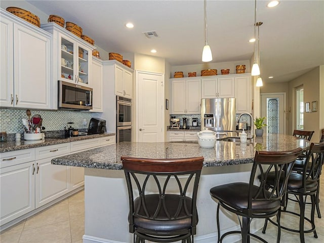 kitchen featuring stainless steel appliances, dark stone counters, pendant lighting, a center island with sink, and white cabinets