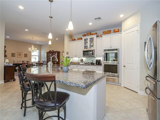 kitchen with appliances with stainless steel finishes, dark stone counters, decorative light fixtures, an inviting chandelier, and white cabinets